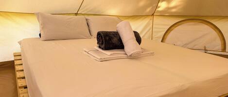 Una cama con sábana blanca, dos almohadas, una toalla enrollada y una toalla doblada.