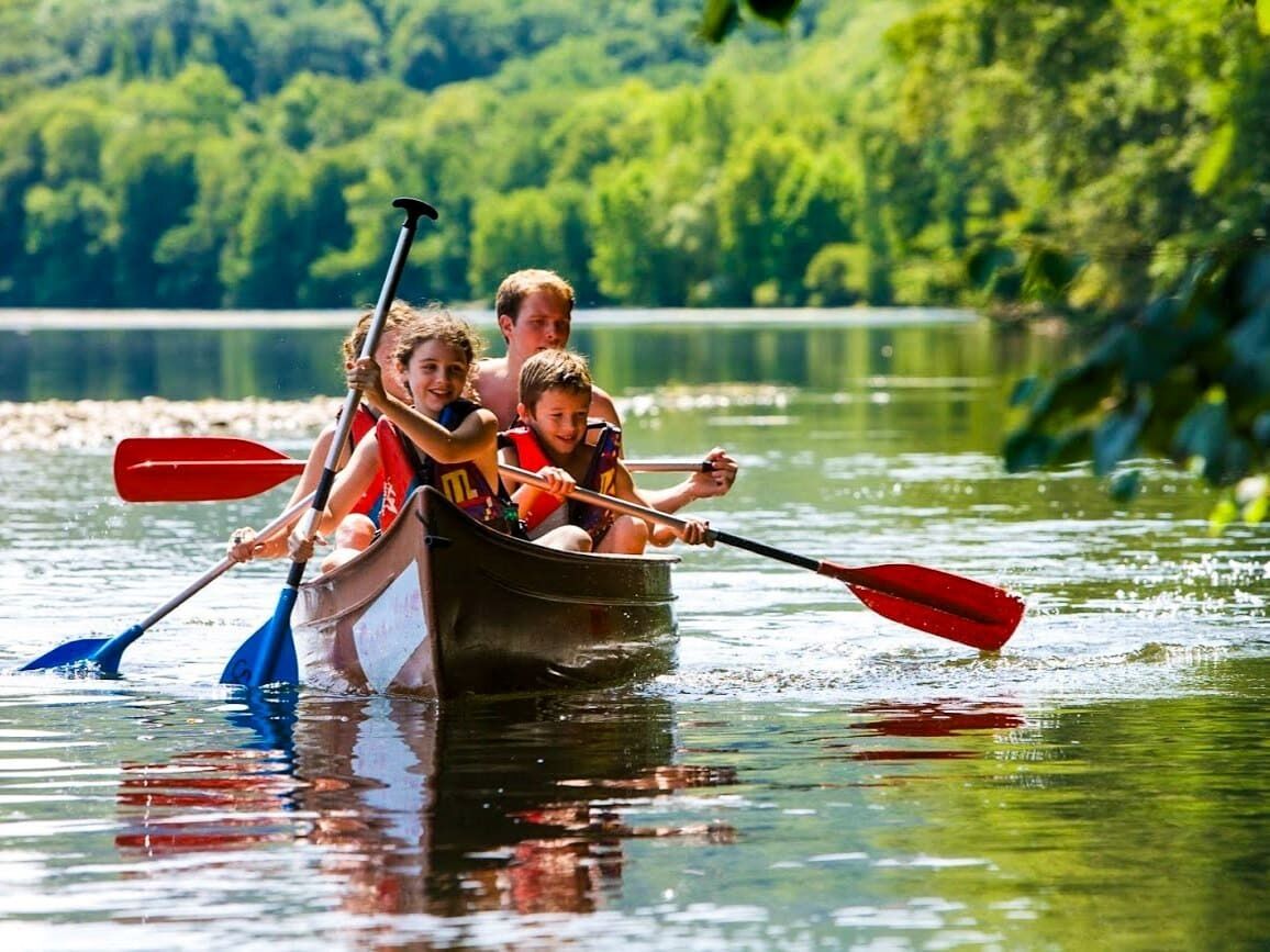 A group of people in a canoe on a calm lake surrounded by lush greenery.