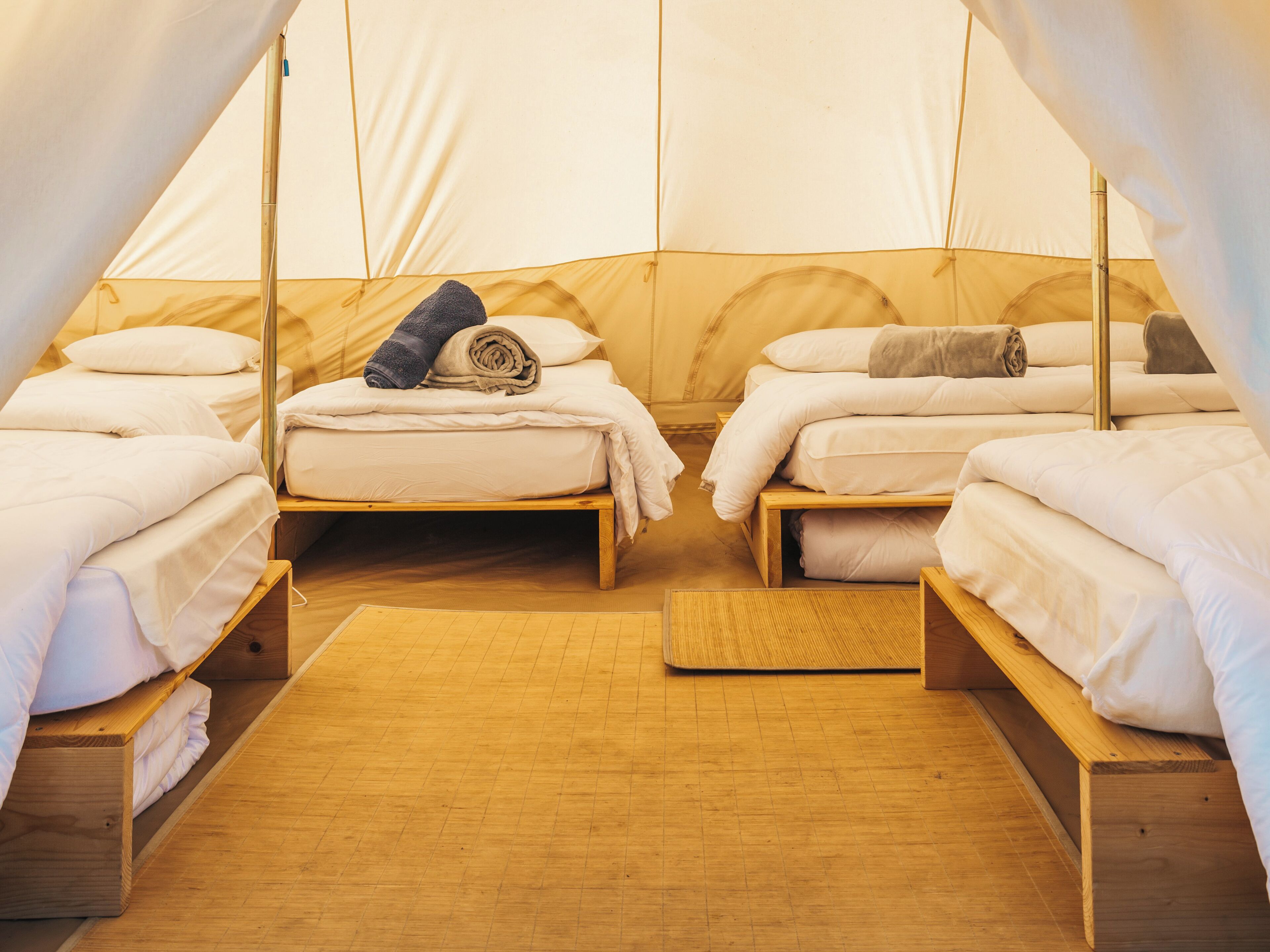 A tent with two beds, each with white bedding and pillows, and a wooden floor.