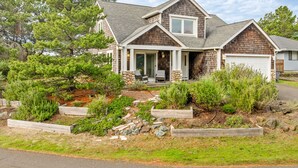A two-story house with a covered porch, stone foundation, and a garage. - Caddy Corner MCA#1122-EV Charger, Golf Course Lake views, 2 blocks to beach. (Manzanita)