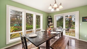 A dining area with a wooden table set for four, large windows, and a chandelier. - Caddy Corner MCA#1122-EV Charger, Golf Course Lake views, 2 blocks to beach. (Manzanita)