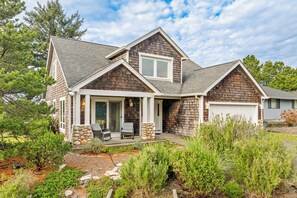 A two-story house with a stone foundation, a covered front porch, and a garage. - Caddy Corner MCA#1122-EV Charger, Golf Course Lake views, 2 blocks to beach. (Manzanita)