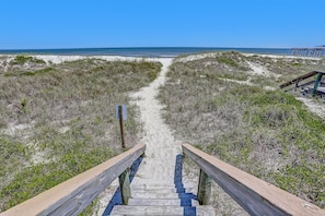 A wooden boardwalk leading to a beach with sand dunes and sparse vegetation.