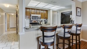Une cuisine avec des meubles de rangement en bois, un four à micro-ondes et une cuisinière. On y trouve trois tabourets de bar avec des assises rembourrées.