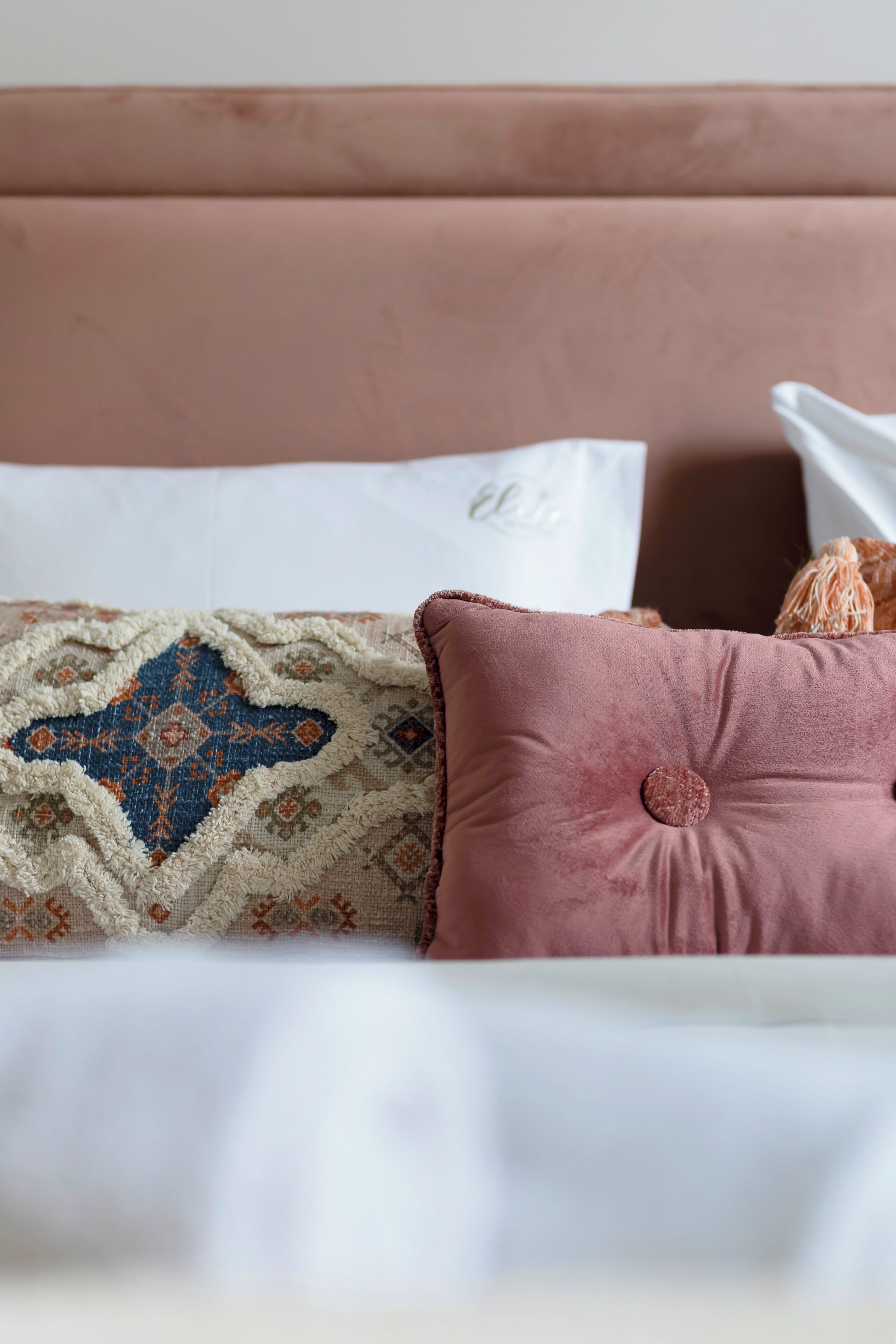 Un lit avec un couvre-lit à motifs, un coussin rose et un coussin blanc portant un nom.