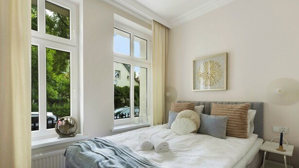 A bedroom with a large bed, a window with curtains, a bedside table, and a wall-mounted artwork. - Elite Apartments Korzeniowskiego seaside (Gdansk)