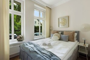 A bedroom with a large bed, a window with curtains, a bedside table, and a wall-mounted artwork. - Elite Apartments Korzeniowskiego seaside (Gdansk)