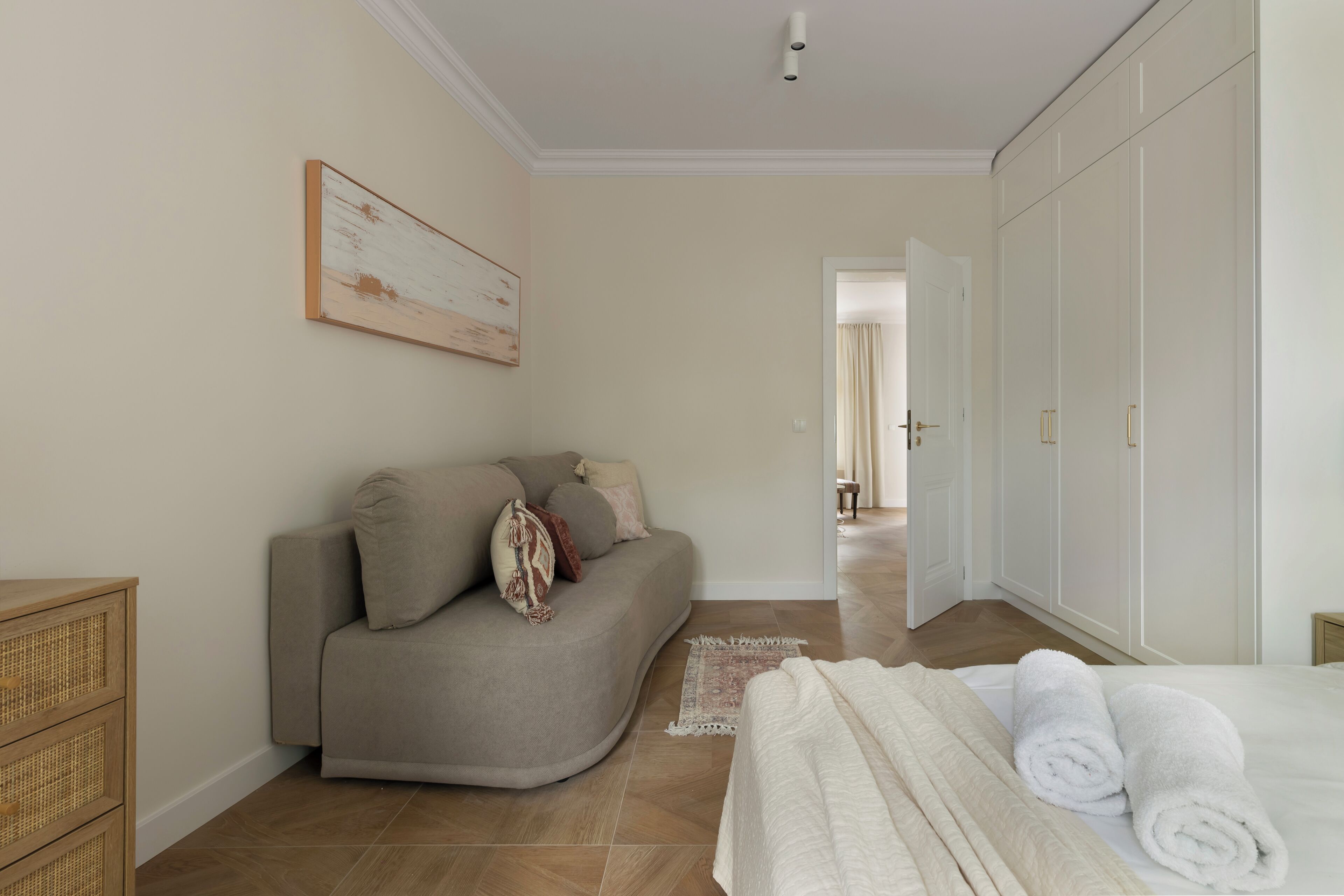 Une chambre avec un canapé, un lit agrémenté de serviettes pliées, une commode en osier et une grande armoire.