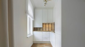 A narrow hallway with white cabinets, a window, and a patterned backsplash. - Elite Apartments Korzeniowskiego seaside (Gdansk)