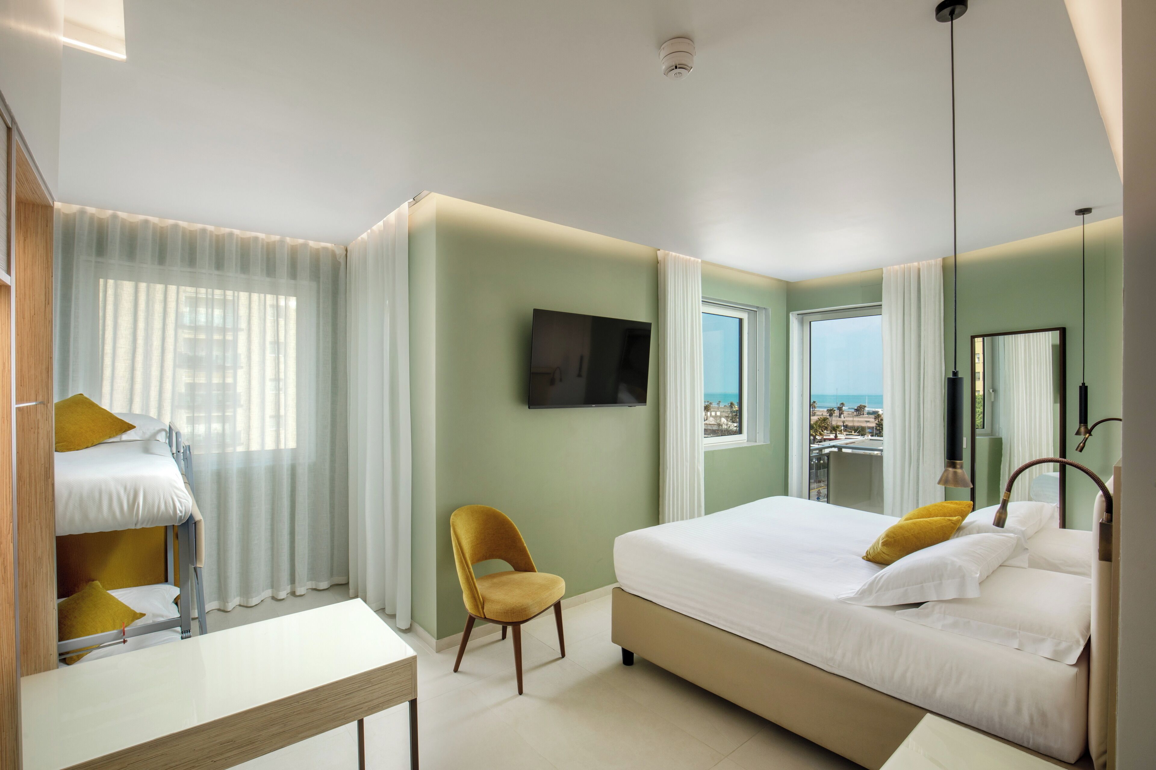 Une chambre d’hôtel avec un lit, un bureau, une chaise, une télévision et une vue sur la mer.