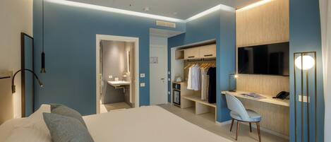 A modern hotel room with a large bed, a desk with a chair, a wardrobe, and a TV.