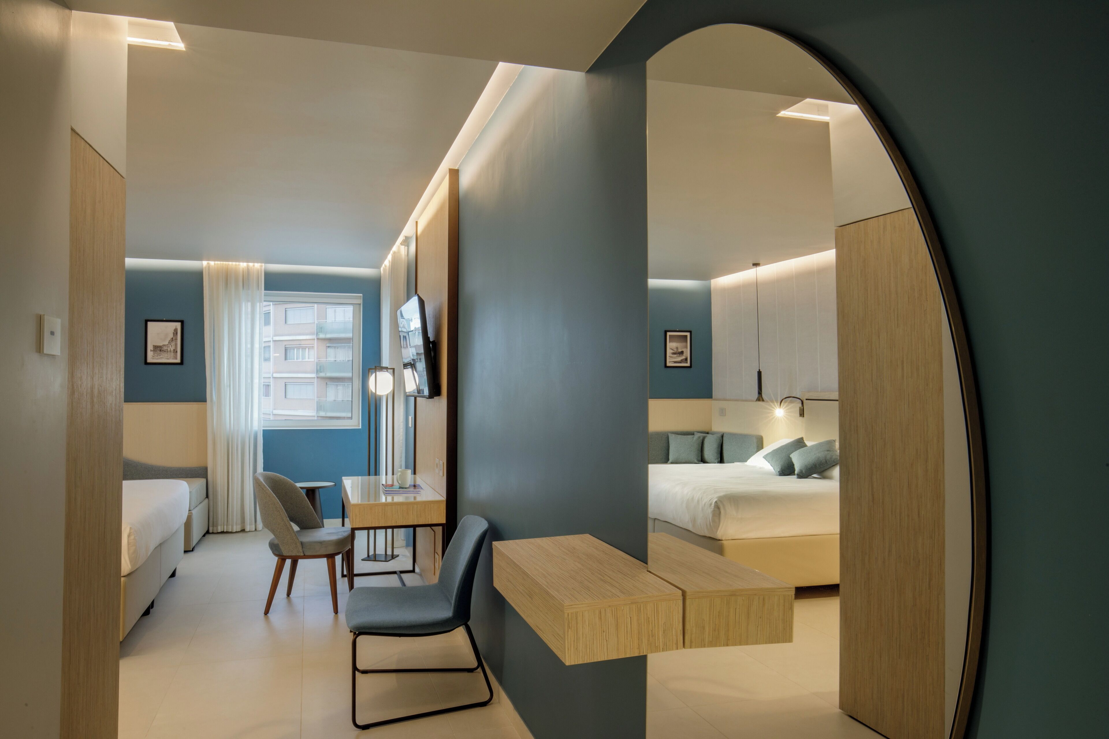 Een moderne hotelkamer met een bed, een bureau, een stoel, een spiegel en een raam.