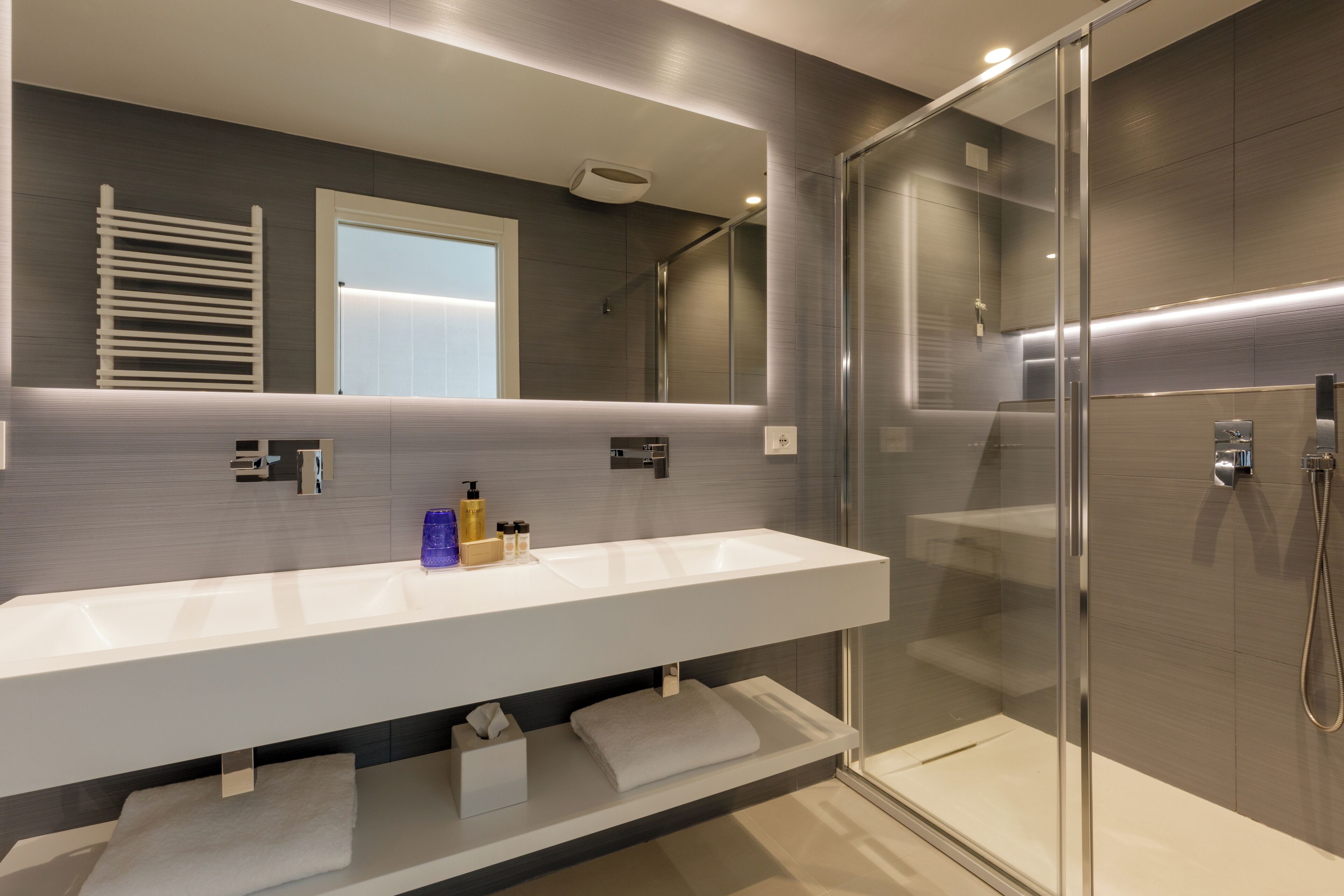 A modern bathroom with a large mirror, a white sink, and a glass-enclosed shower.