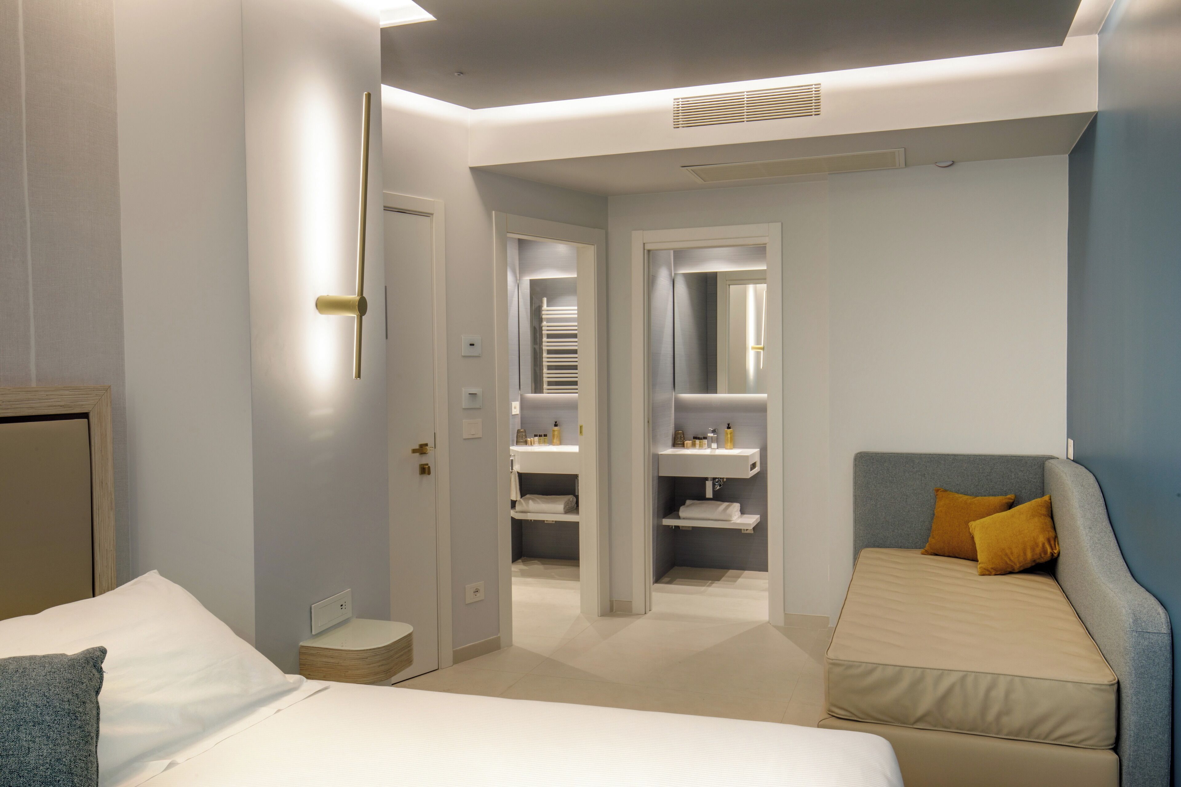 A modern hotel room with a bed, a small sofa, a walk-in closet, and a bathroom.