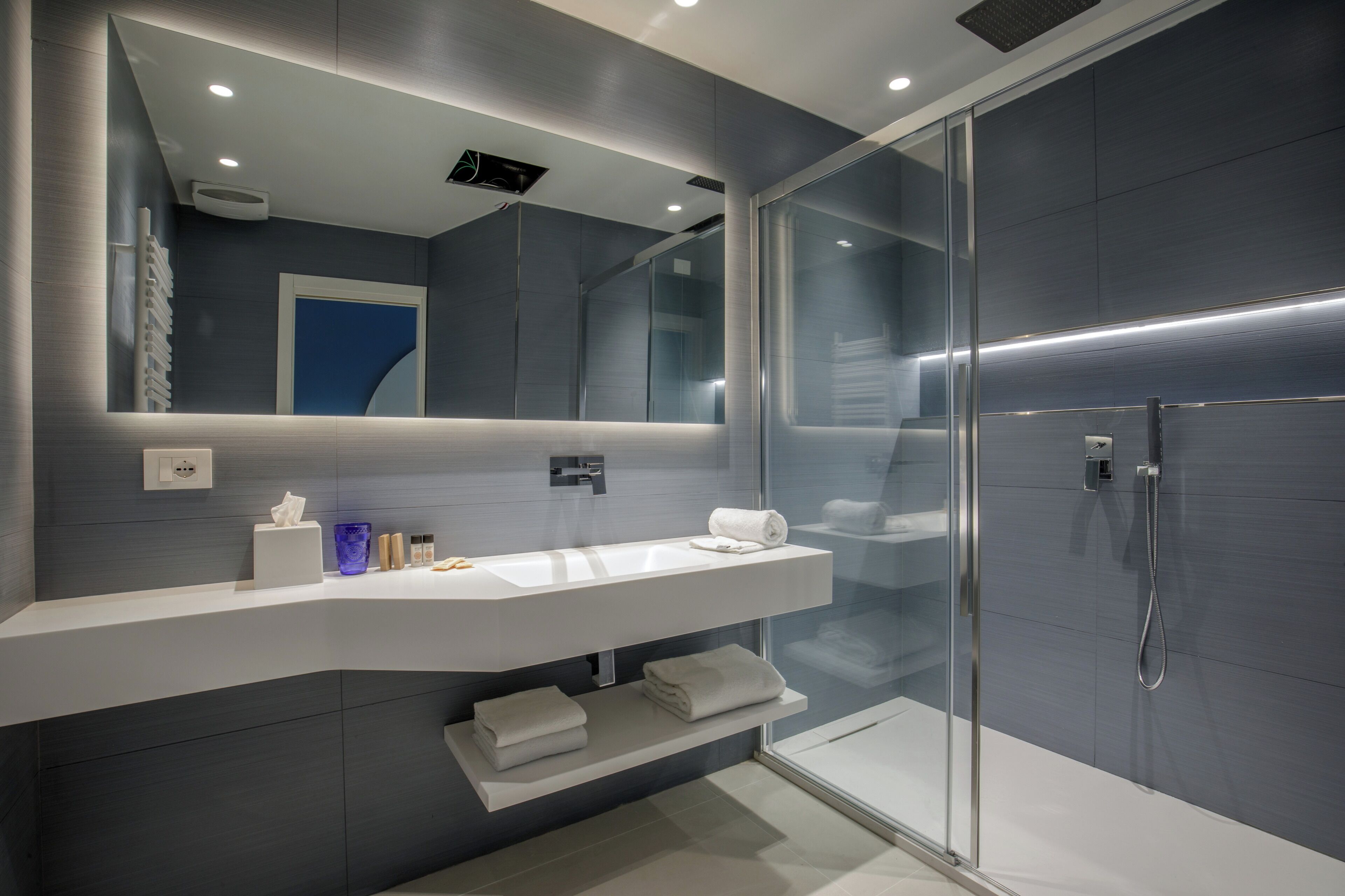 Une salle de bain moderne avec une douche à parois de verre, un meuble-lavabo blanc avec un miroir et un porte-serviettes.