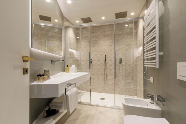 Un baño moderno con ducha envuelta en vidrio, un lavamanos blanco y un inodoro.