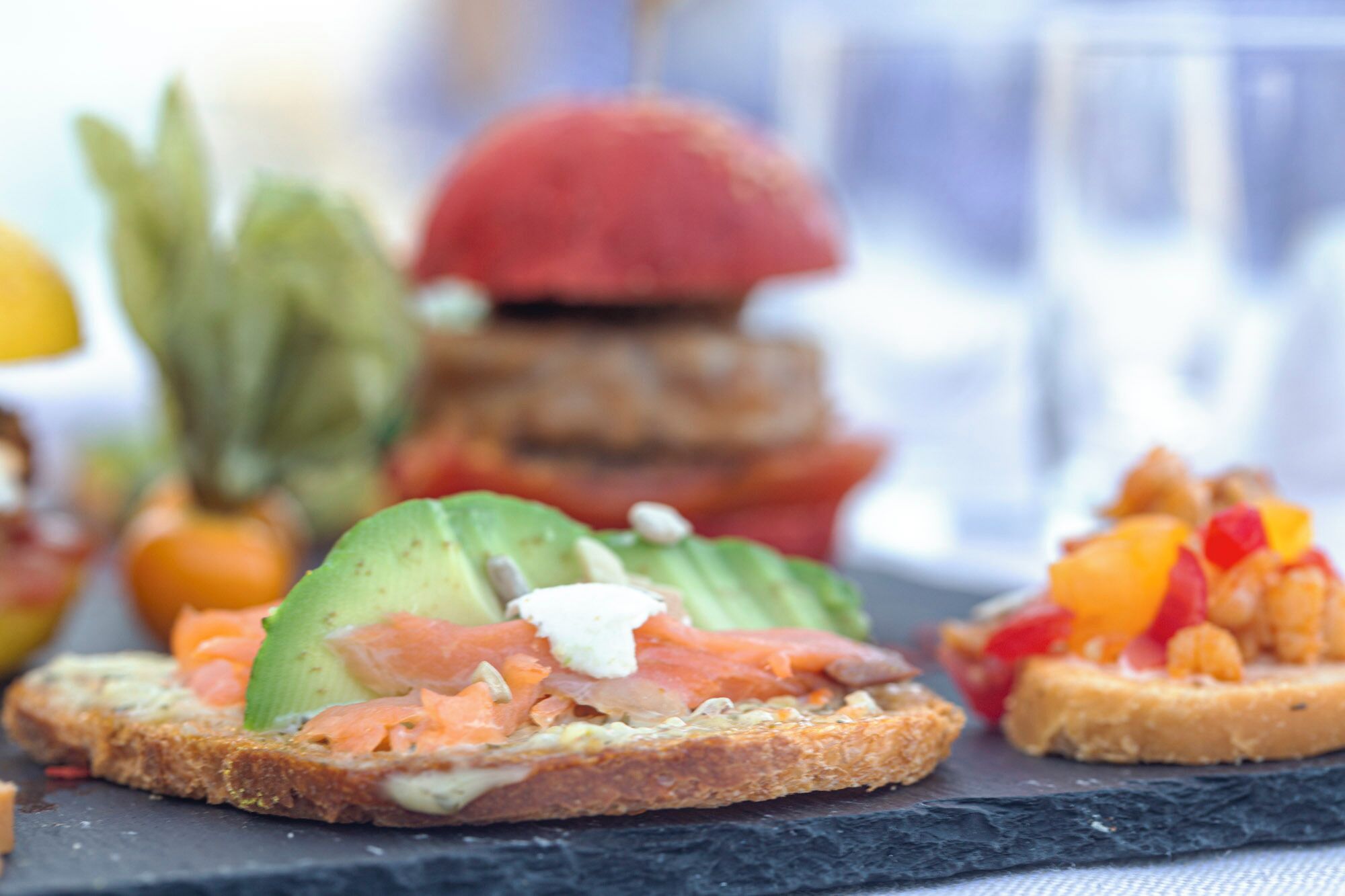 A variety of appetizers on a slate board, including avocado toast, smoked salmon, and a fruit salad.