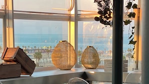 En restaurang med genomskinliga stolar i glas, träbord och utsikt över havet.