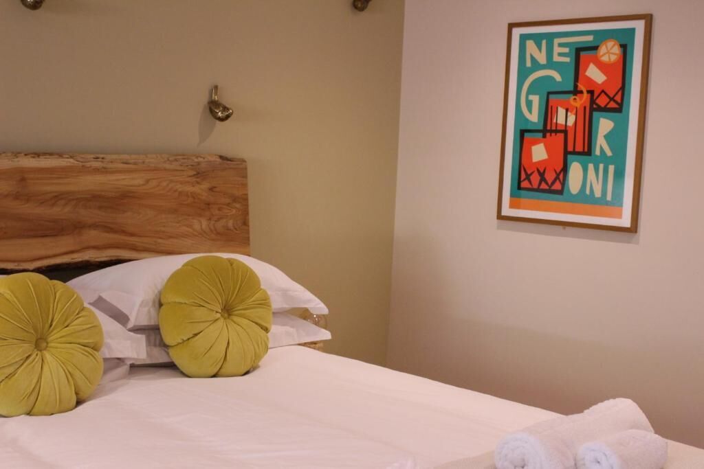 Un lit bien fait, avec du linge de lit blanc et deux grands oreillers jaunes, une tête de lit en bois et une œuvre d’art encadrée accrochée au mur.