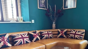A cozy living room with a brown leather sofa adorned with British flag cushions, two copper round tables, and a teal wall with framed pictures. - The Kings Head Inn  (Norwich)
