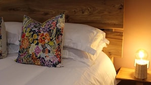 A bed with white linens and a floral pillow, a wooden headboard, and a bedside lamp. - The Kings Head Inn  (Norwich)