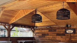 A covered outdoor seating area with wooden benches and tables, a wooden ceiling, and hanging light fixtures. - The Kings Head Inn  (Norwich)