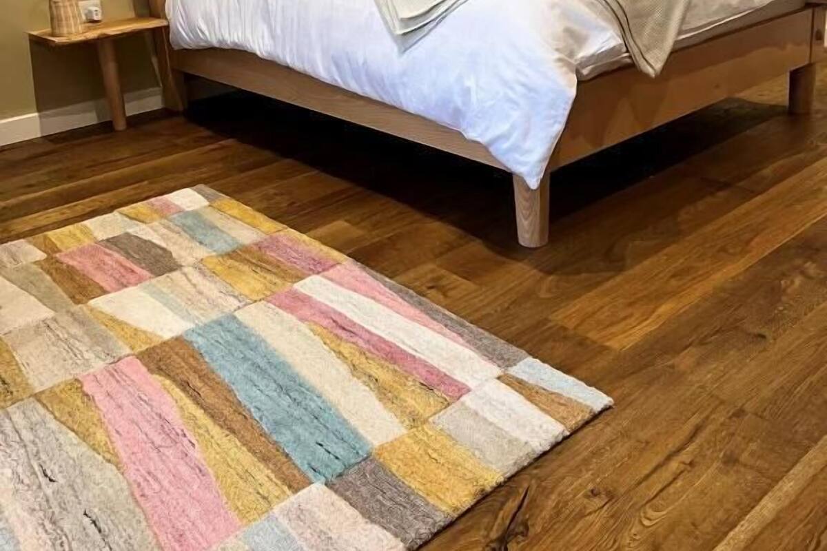 Un dormitorio con una cama de madera, un tapete a rayas de colores y una obra de arte en la pared.
