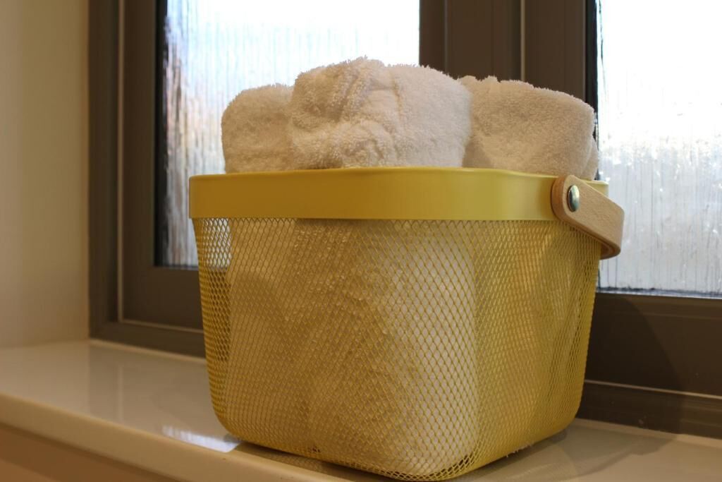 A yellow mesh laundry basket with a handle, containing folded white towels, placed on a windowsill.