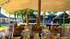A table set with bread and glasses under a canopy, with a view of a garden and buildings in the background. - Lodging Nature Camp Châteaux de la Loire (Cellettes)