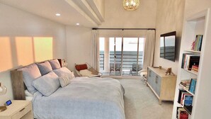 A modern hotel room with a large bed, a seating area with a view, and a bookshelf. - Beachfront Estate - LB Peninsula (Long Beach)