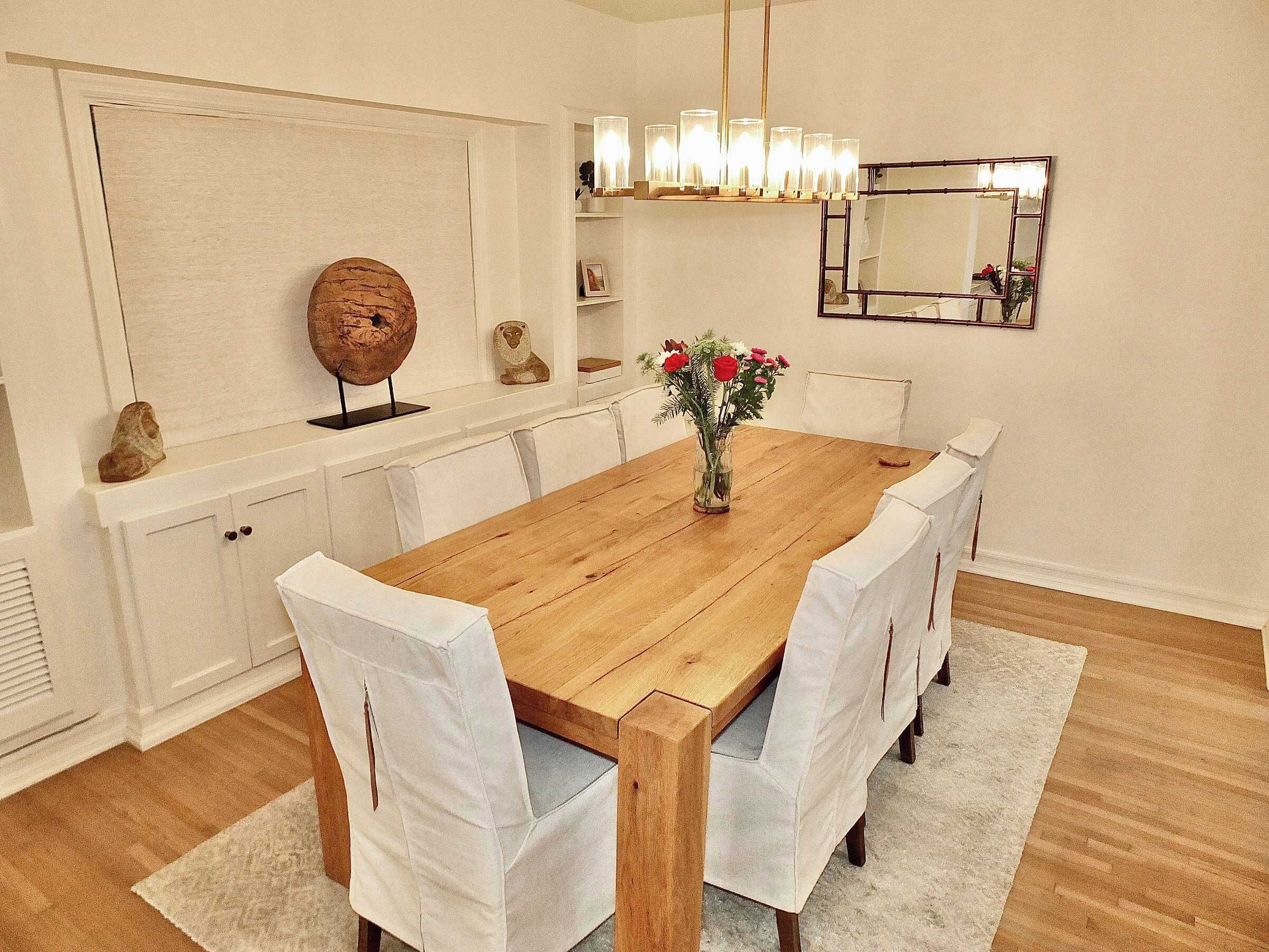A dining room with a wooden table, white chairs, a vase with flowers, a globe, and a mirror on the wall.