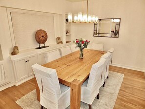 A dining room with a wooden table, white chairs, a vase with flowers, a globe, and a mirror on the wall. - Beachfront Estate - LB Peninsula (Long Beach)