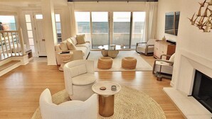 A modern living room with a large window, a fireplace, and a balcony with a view of the sea. - Beachfront Estate - LB Peninsula (Long Beach)