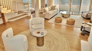 A spacious living area with a large window overlooking the sea, a staircase, and a modern sofa. - Beachfront Estate - LB Peninsula (Long Beach)