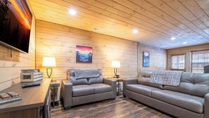 A cozy cabin interior with two leather sofas, wooden walls, and a TV mounted on the wall.
