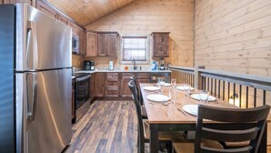 A compact kitchen with wooden walls, a stainless steel refrigerator, a microwave, and a dining table set for four.