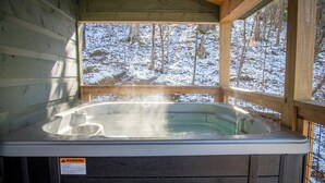 A hot tub in a wooden cabin with a warning label, surrounded by a snowy forest.