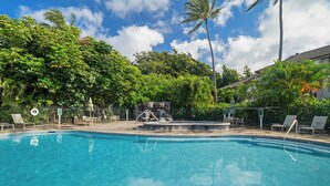 A clear blue pool surrounded by lush greenery and palm trees, with lounge chairs and a small waterfall feature. - Aston Poipu Kai Kauai 114 | Garden View Retreat – Pool & Hot Tub (Koloa)