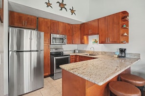 A kitchen with wooden cabinets, stainless steel appliances, a granite countertop, and a small island with stools.