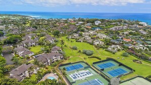 An aerial view of a residential area with houses, green spaces, and tennis courts.