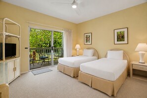 Een hotelkamer met twee bedden, een televisie, een balkon met uitzicht op groen, en twee schilderijen aan de muur.