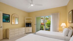 Une chambre d’hôtel avec deux lits, une télévision, une commode, un ventilateur de plafond et un balcon donnant sur un paysage verdoyant.