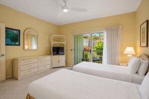 Een hotelkamer met twee bedden, een televisie, een dressoir, een plafondventilator en een balkon met uitzicht op groen.