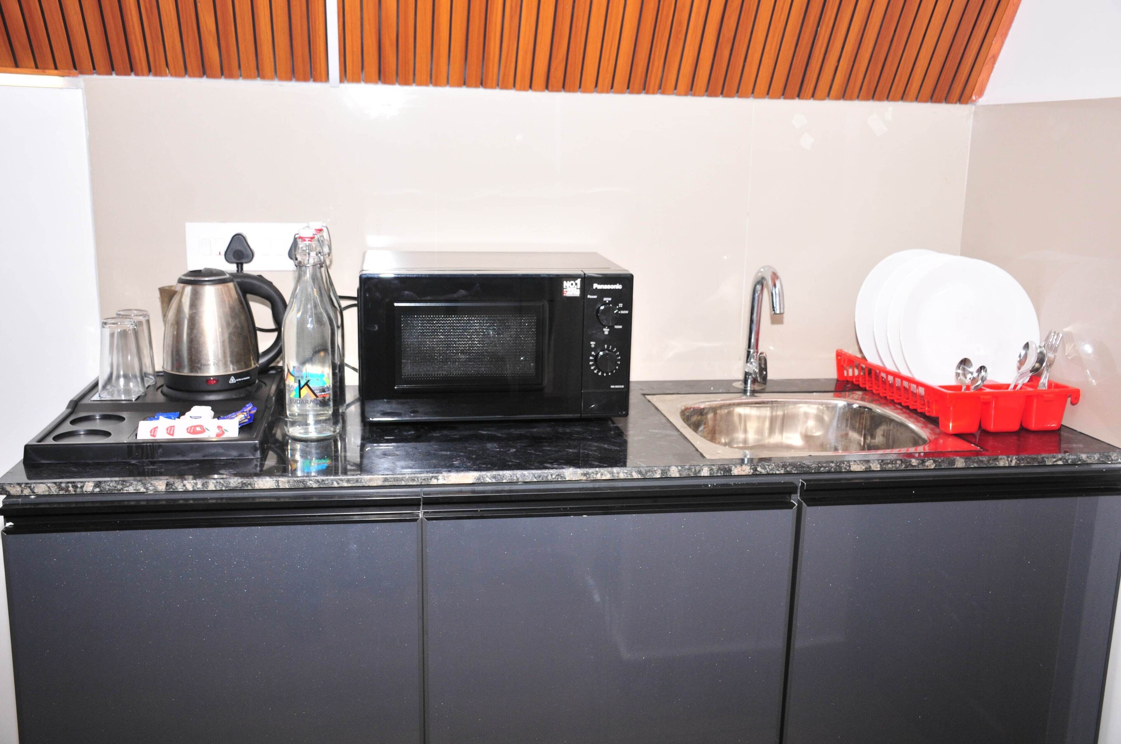 Una cocina con microondas, hervidor, pileta y escurreplatos.