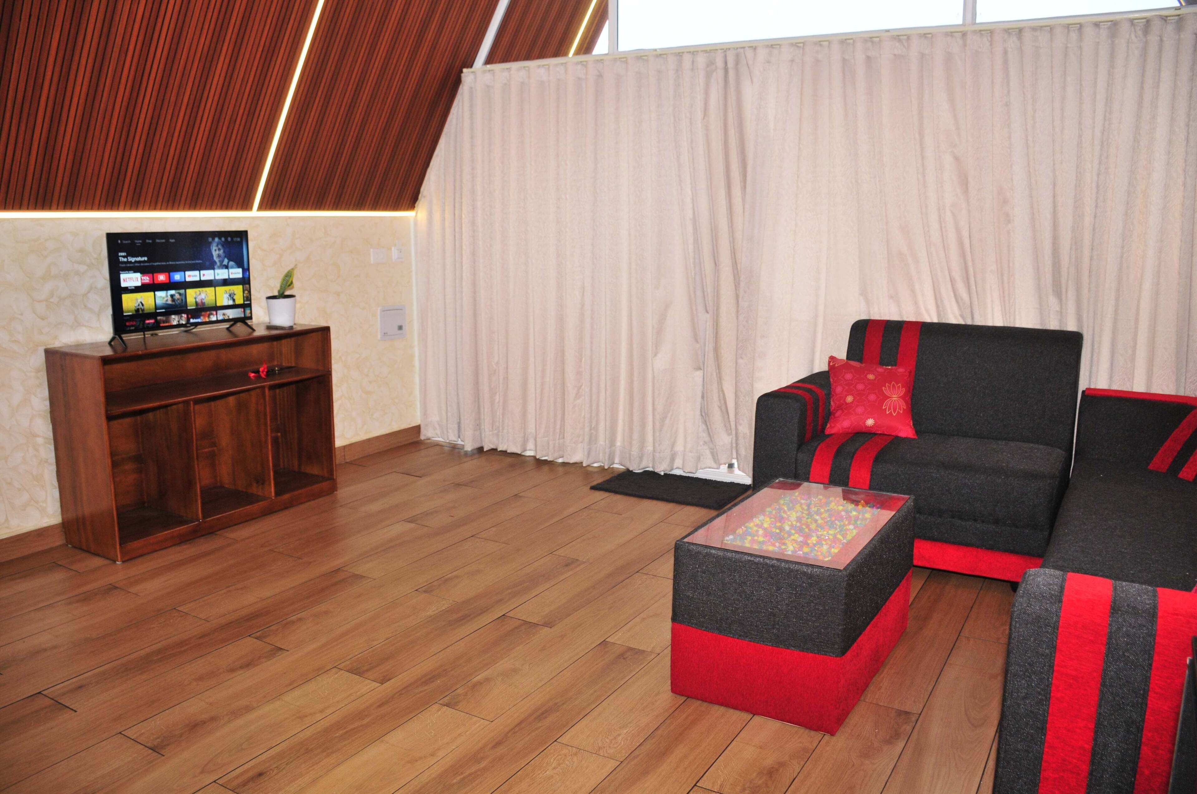 Een moderne woonkamer met een flatscreen televisie, een houten tv-meubel, een zwart-rode bank en een glazen salontafel.