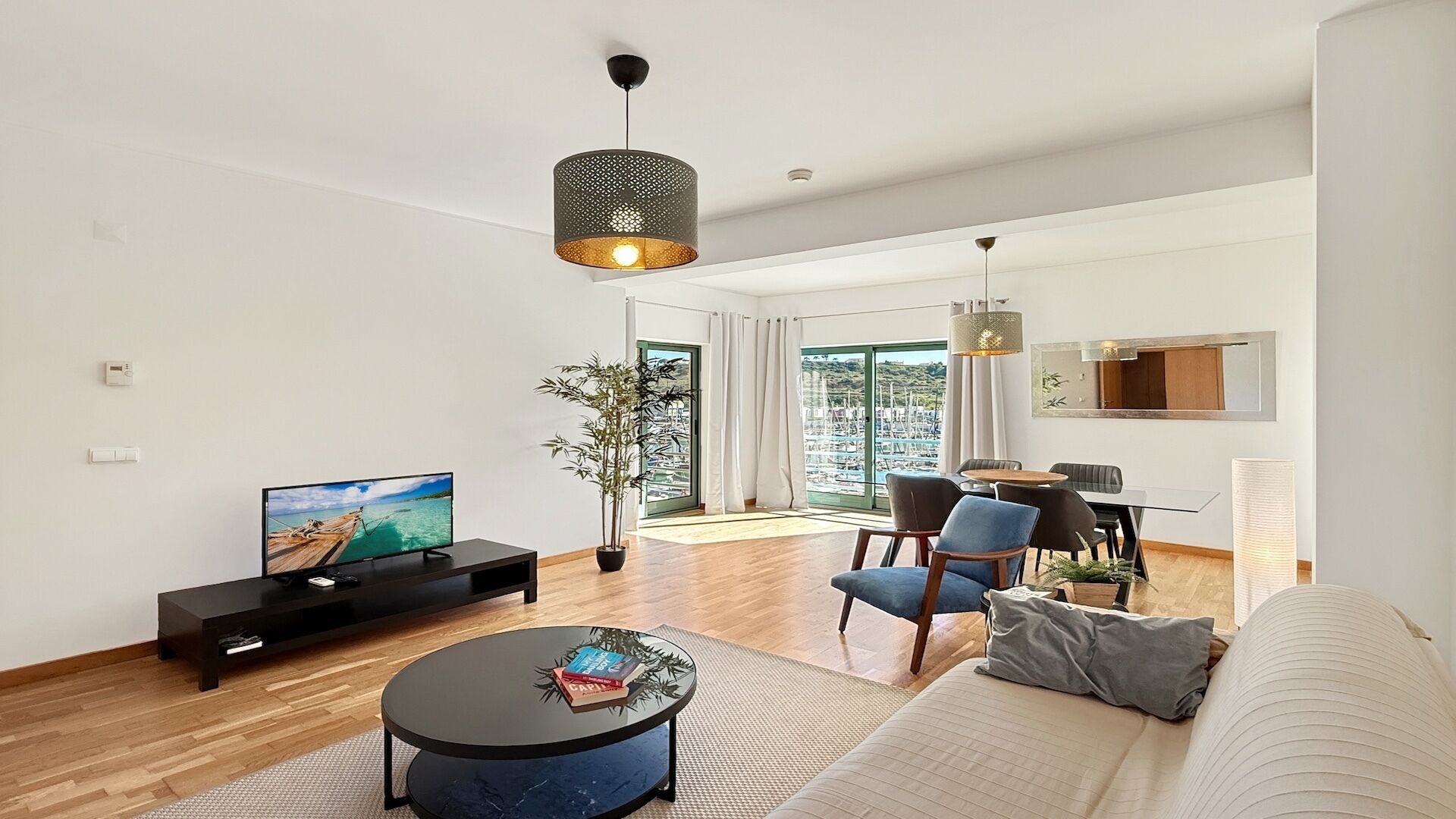 Una sala de estar moderna con un televisor de pantalla plana, una mesa redonda, un sofá y una zona de comedor con sillas y una mesa.