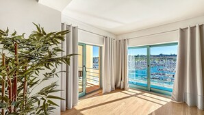 Amplia habitación con ventanas grandes, vista a un puerto deportivo y una planta de bambú.