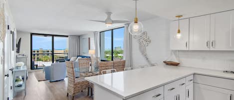 A modern kitchen with white cabinetry, a central island, and a dining area with wicker furniture.