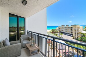 A balcony with wicker furniture, a view of the beach, and a parking area.