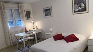 Un dormitorio con cama, escritorio, silla, mesita de noche y ventana con cortinas.